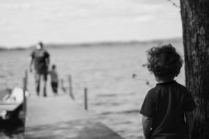 Child watches alone as adult and child walk away down a dock over water