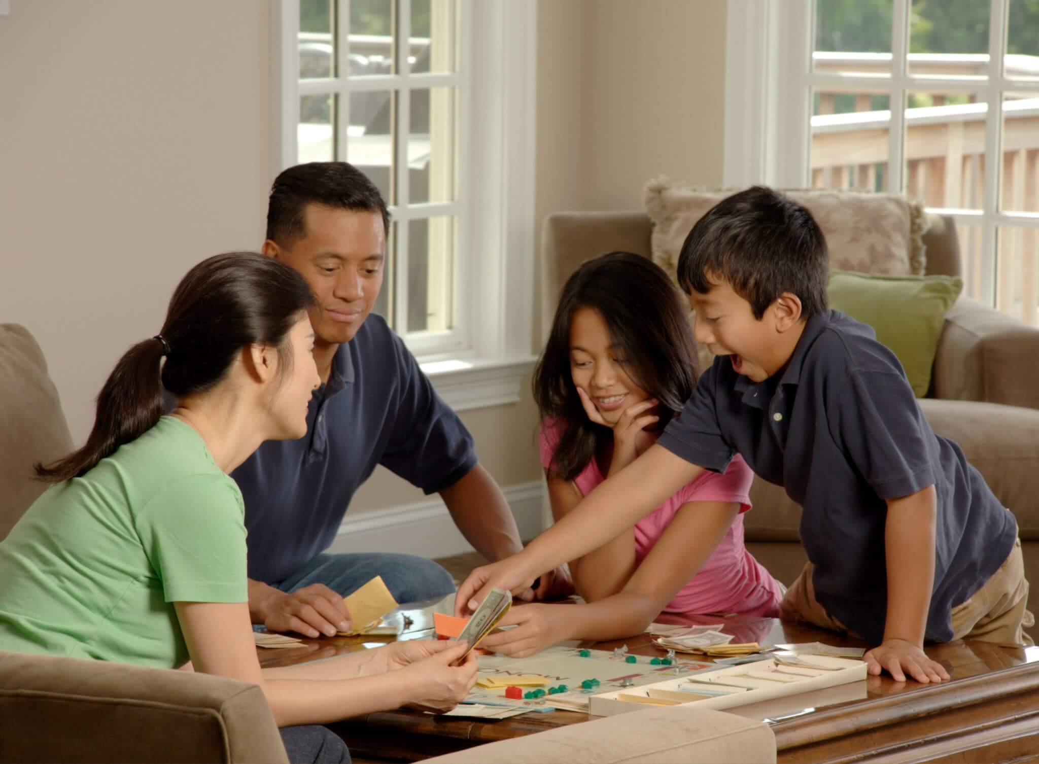 A family playing a board game and smiling around a coffee table in a bright and neutral-colored living room.