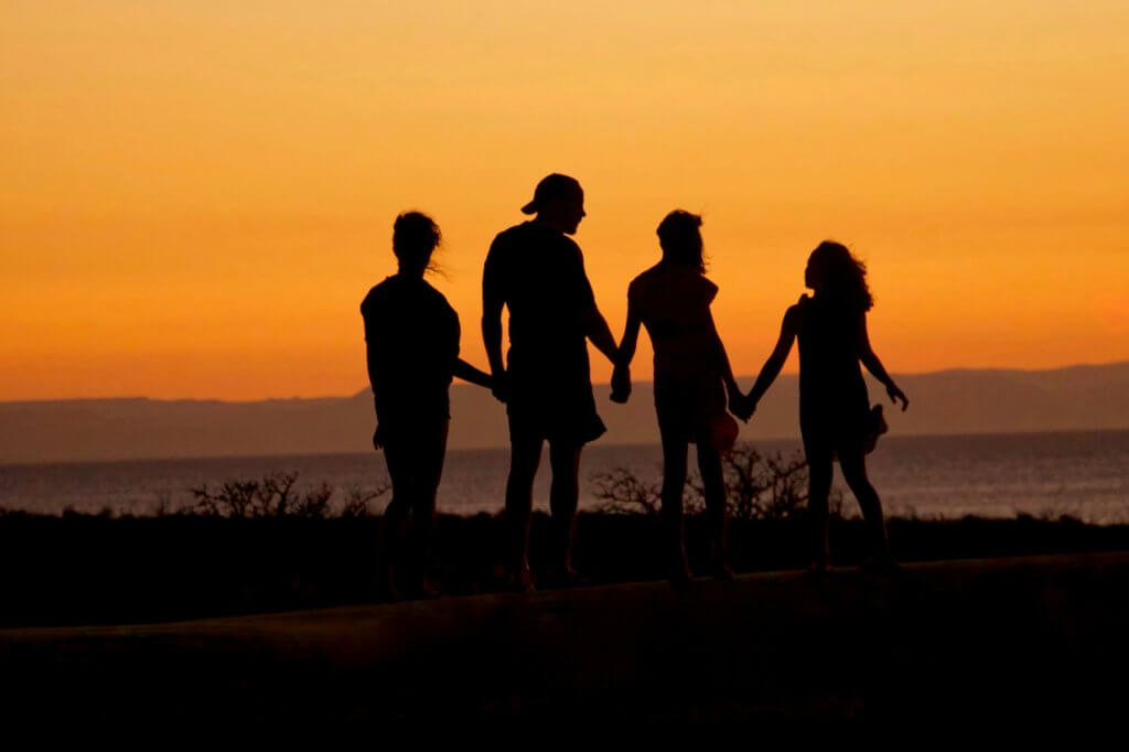 A family of two parents and two children stands silhouetted against an orange sunset
